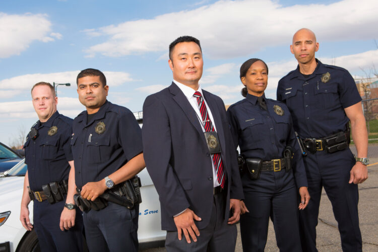 Photo of a group of diverse law enforcement officers standing in a line in front of a police care